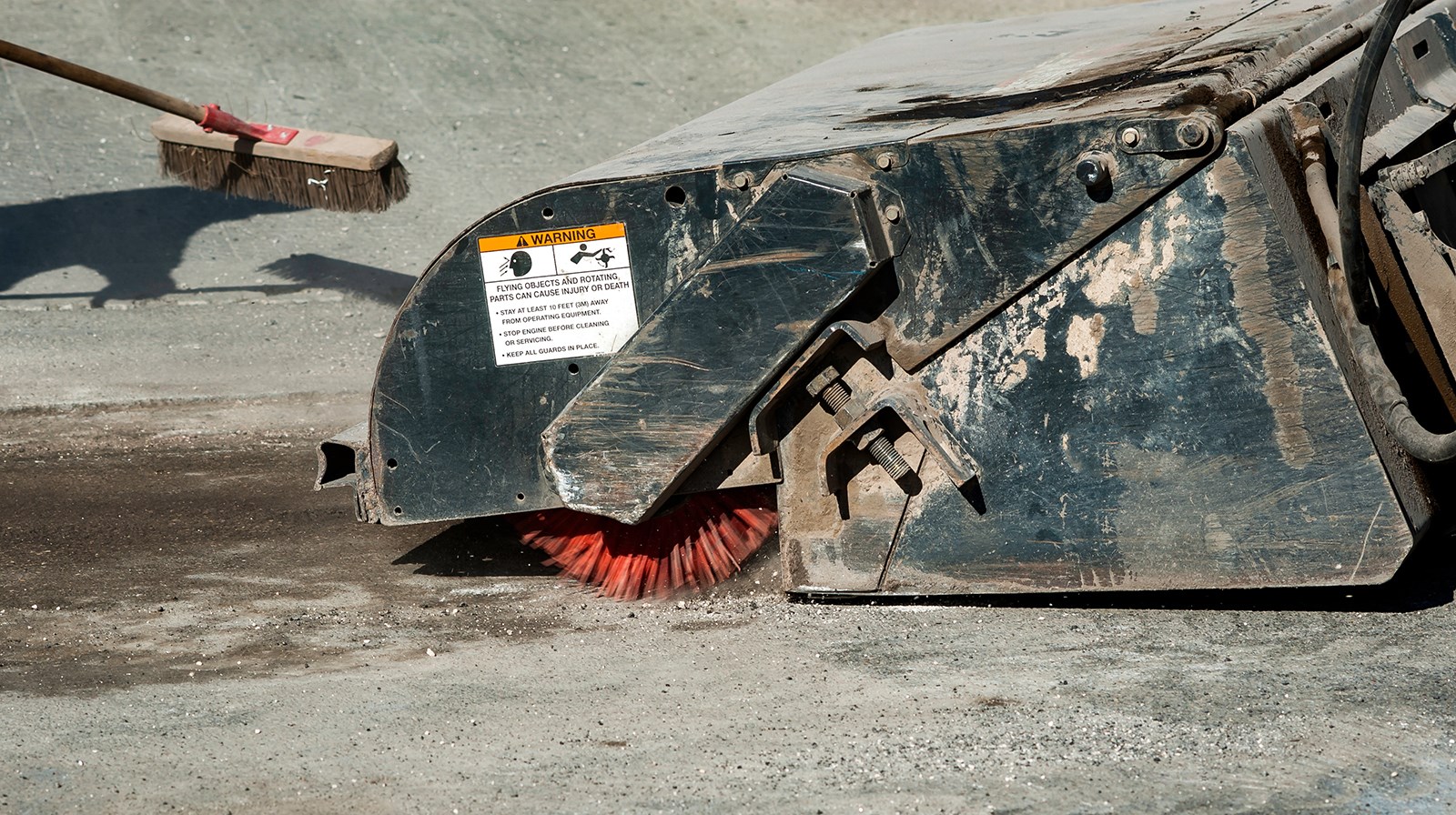 Närbild på en maskin som sopar upp grus på asfalt. 