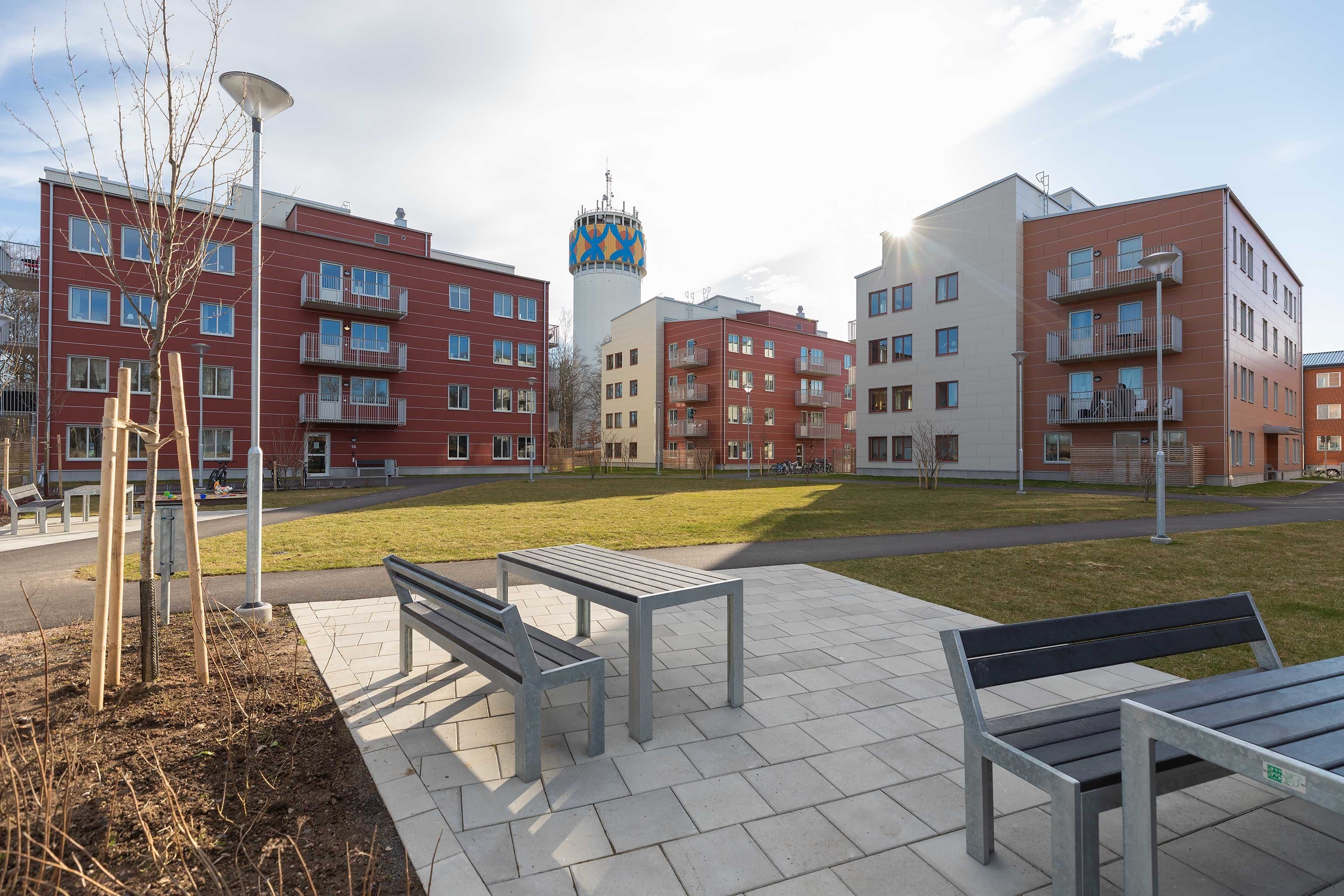 Kvartersbild över Kv Haganäs 3, tre 4våningshus i beige och rött med soffgrupper i framkant. Fotogr