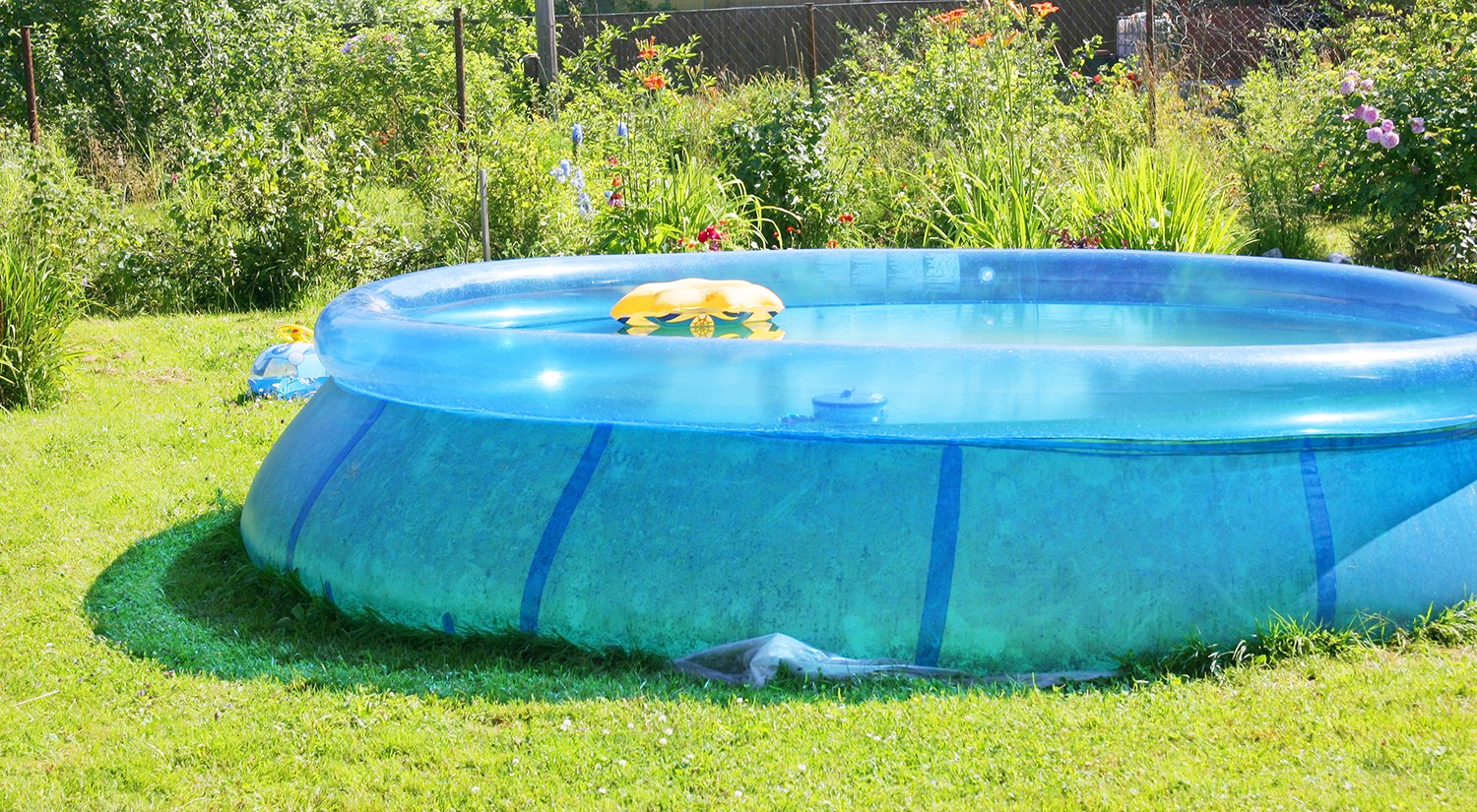 Stor pool i blått som står på en gräsmatta med en gul badring i. 