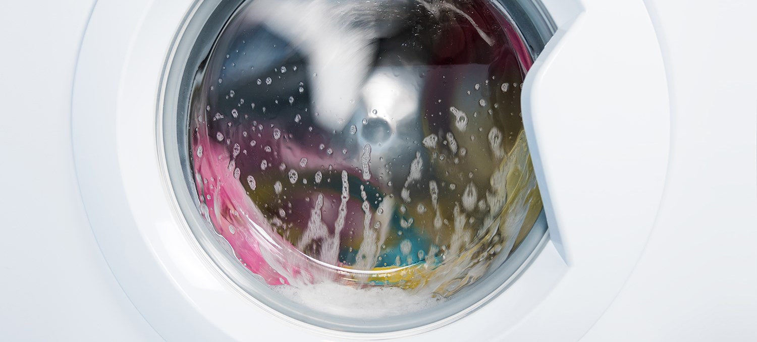 Luckan på en vit tvättmaskin där kläder tvättas. 