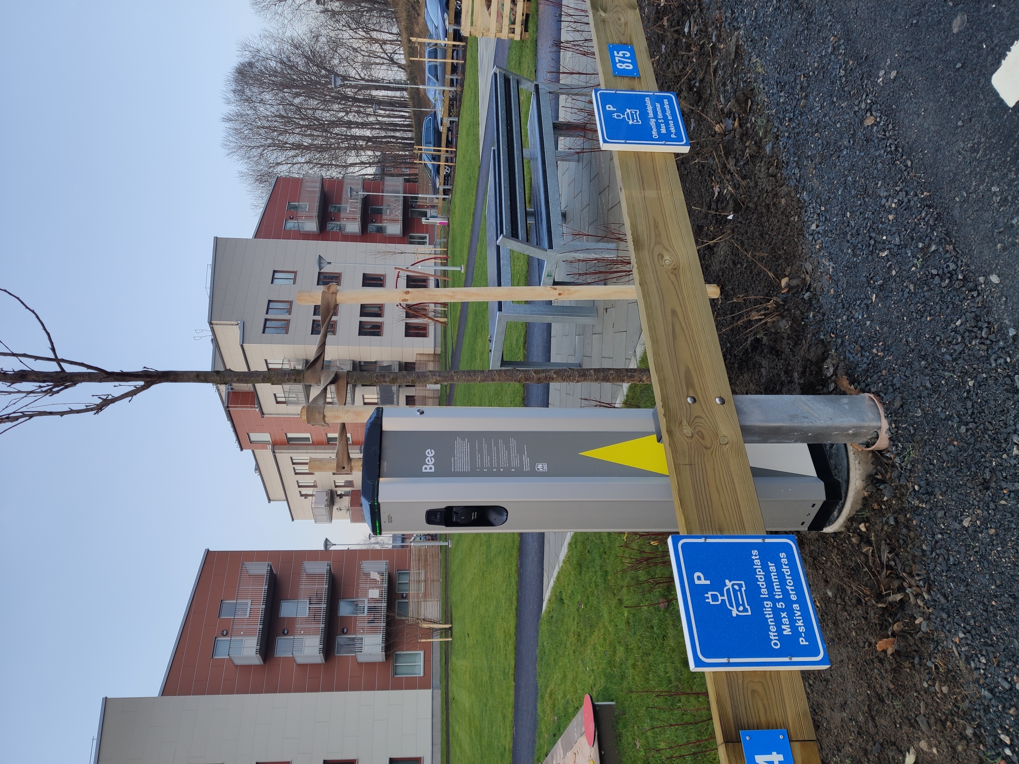 Elbilsladdare på parkering med flerfamiljshus i bakgrunden.